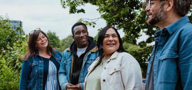 Four people in a leafy outdoor environment smiling and chatting