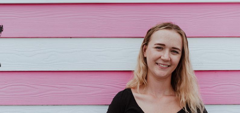 A person smiling against a pink stripe background 