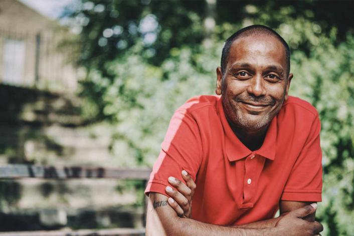 A smiling man standing in front of green leaves 