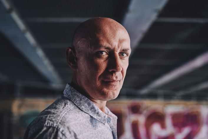 man with a straight face in front of some graffiti under a bridge